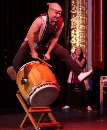 taiko artist Mark H Rooney jumps over a drum