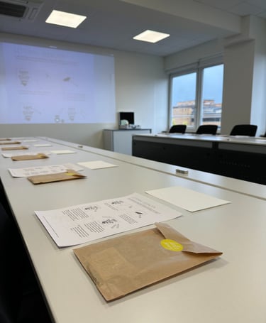 Hand lettering workshop materials including instructional sheets and brown paper bags on white tables in a classroom.