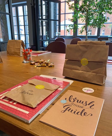 Brush lettering guide and brown paper gift bags on a wooden table at a creative workshop.