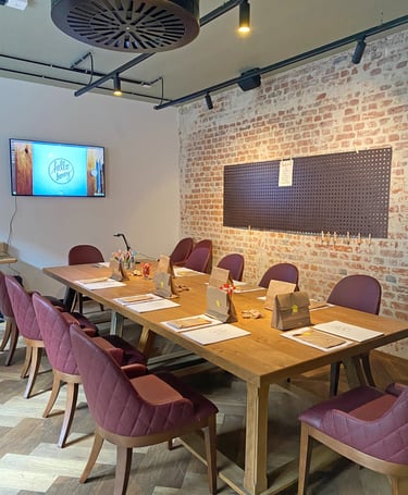 A rustic meeting room with a wooden table, burgundy chairs, and an exposed brick wall.