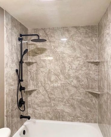 Modern bathtub and shower combination featuring marble-look wall panels, matte black rainfall showerhead, and built-in corner