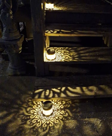 Solar lanterns casting decorative mandala patterns on outdoor wooden garden steps at night.