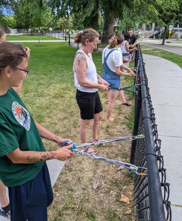 A group of people typing climbing anchors on a park fence
