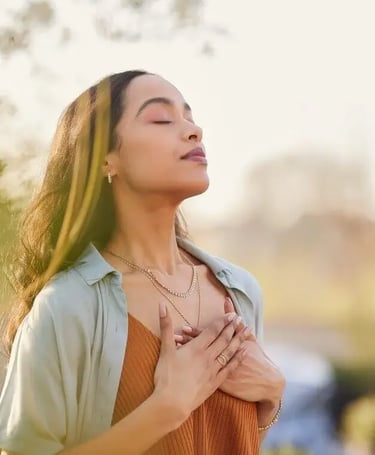 Une femme respire profondément en se tenant debout à l'extérieur, savourant un moment de sérénité et de connexion.