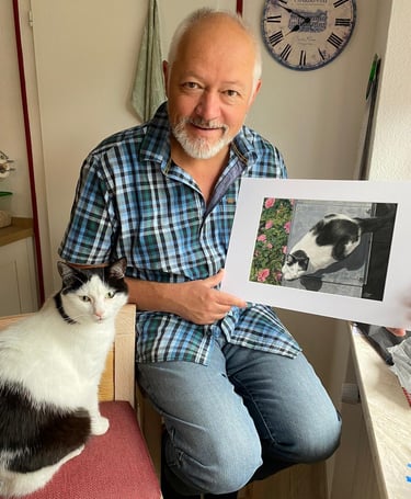 a man holding a pastel painting of his cat, with his cat sitting next to him