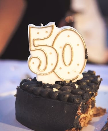 A 50th birthday candle with gold trim on a slice of gourmet dark chocolate cake.