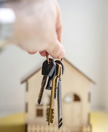 Una mano sosteniendo un manojo de llaves, una casa al fondo