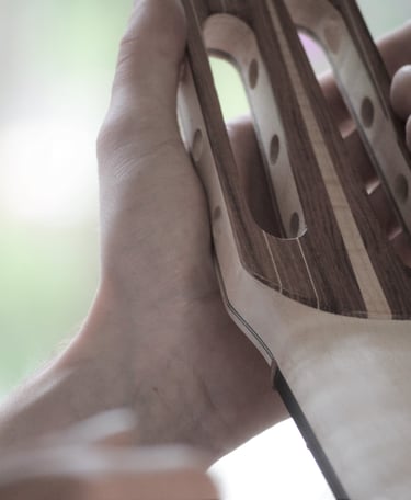 A luthier holding a handcrafted wooden 7 string guitar headstock during the assembly process.