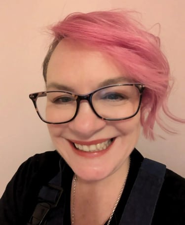 Smiling woman with bright pink hair and tortoiseshell glasses in a close-up portrait.