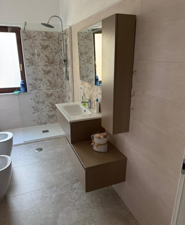 Modern bathroom featuring a floating vanity, walk-in shower with floral tile, and stone flooring.