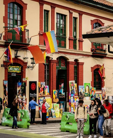 Local paintings displayed for sale outside a colonial house with visitors walking in La Candelaria town