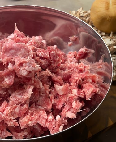 Raw ground Italian sausage in a bowl with chopped mushrooms and burger buns, ready for cooking a hearty meal.