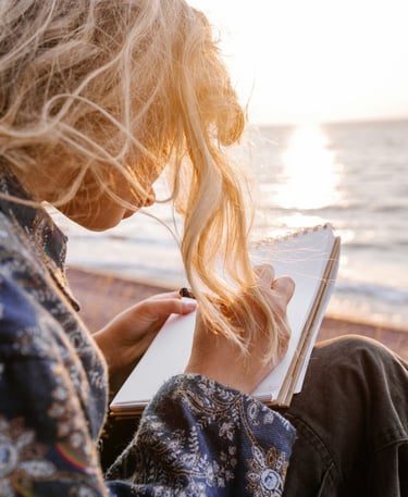 Femme écrivant son journal de gratitude assise à la plage"