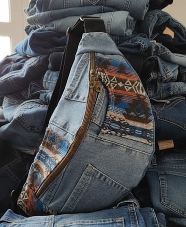 Sac banane en denim bleu et motifs colorés posé sur un tas de vêtements en jean