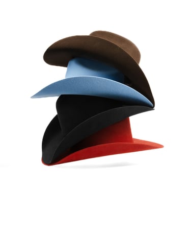 A stack of colorful wide-brimmed felt fedora hats in brown, light blue, black, and red.
