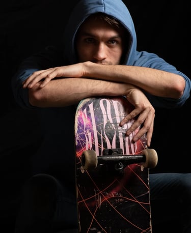 Un jeune homme vêtu d'un sweat à capuche bleu, assis avec un skateboard entre les bras