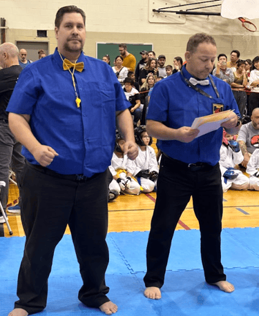 two men standing on a blue mat with a man in a blue shirt