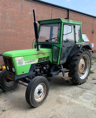 A vintage green Deutz D 7807 C tractor parked on concrete outside a red brick building.