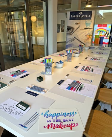Faber-Castell art workshop table set with colorful Pitt Artist Pens, brush markers, and calligraphy paper.