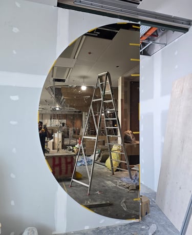 A circular mirror reflecting a construction site with a silver step ladder and drywall installation.