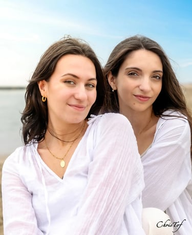 Portrait de deux soeur souriantes portant des hauts blancs légers, posant en extérieur devant la mer
