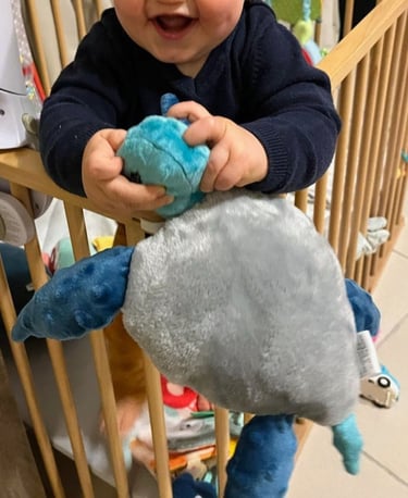 Bébé tenant et manipulant une peluche artisanale dans son lit