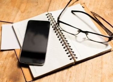 Carnet, lunettes et téléphone illustrant la prise de rendez-vous et les moyens de contact