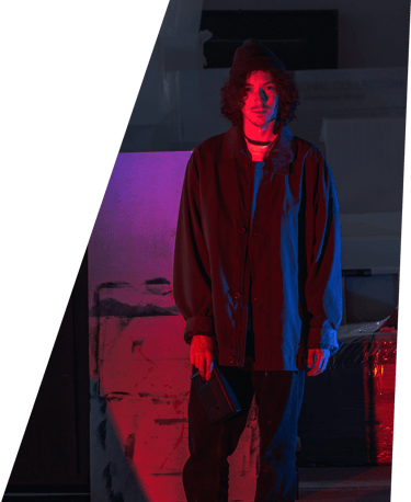 A dark portrait photographic image of In Videcolour lead-songwriter Sam Auckland. Sam is standing, red and blue light on him.