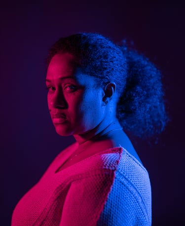 A woman's dramatic profile portrait with vibrant pink and blue neon lighting in a studio.