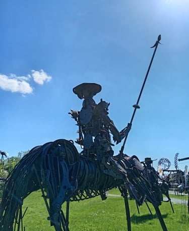 Rustic metal sculpture of Don Quichotte on a horse holding a spear in an outdoor art garden.