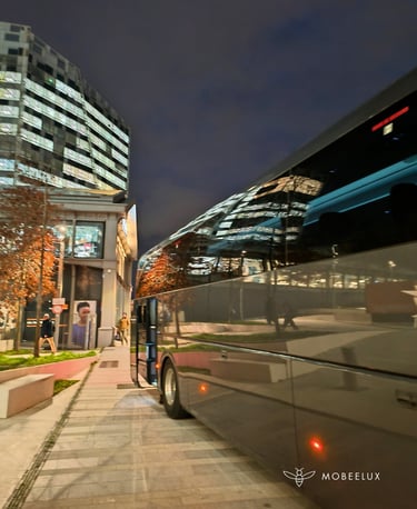 Luxury coach bus parked at night near a modern city office building with glowing window reflections.