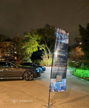 Luxury chauffeur service sedan parked at night next to a MOBEELUX promotional banner.
