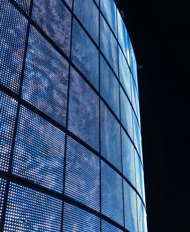 Extreme close-up of a large curved LED panel array in a darkened installation space, electric blue and white LED pixels illuminating the precise seam geometry and curve radius along the panel's edge, nighttime controlled lighting, no ambient fill, architectural framing from a low oblique angle showing depth and curvature