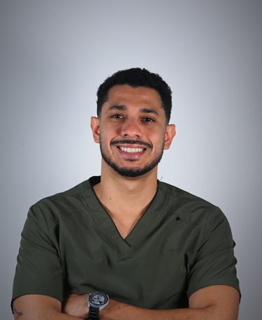 A smiling male healthcare professional wearing olive green medical scrubs against a neutral background.
