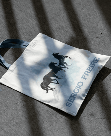 Totebag en el suelo con un diseño de caballos y el logo de Sergio Freire en azul