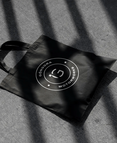 Totebag negra sobre el asfalto con el logo de Góngora Motorworks en blanco