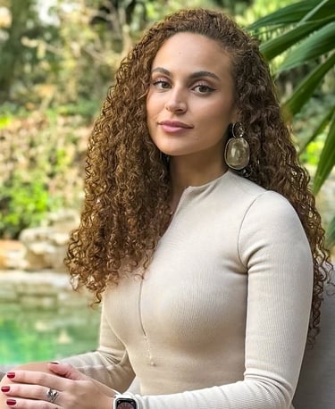 Dalli, founder of The Studio D, sitting outdoors in a cream top with curly hair and statement earrin