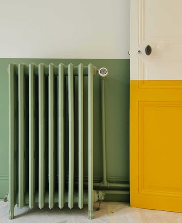 Sage green cast iron radiator against a matching half-painted wall next to a yellow door.