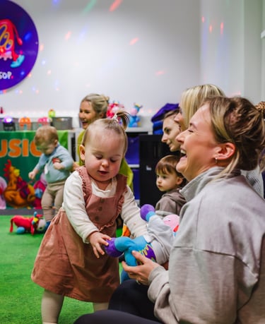 A young Mini Moo attendee and her Mum smiling and laughing, playing with a soft toy.