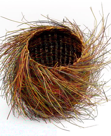 Hand-woven organic nest basket made from colorful pine needles and natural fibers on a white background.