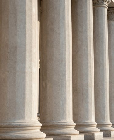 Close-up of classic stone columns of a courthouse, soft natural lateral afternoon light, clean architectural lines, minimalist composition.