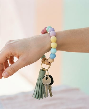 Close-up of a hand wearing a colorful silicone bead keychain wristlet, bright natural daylight, shallow depth of field, pastel background, matte texture of beads.