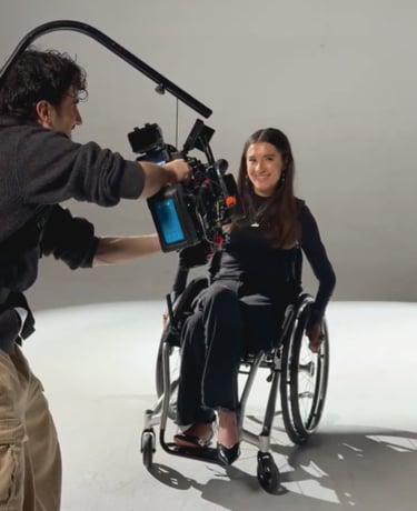 A smiling woman in a wheelchair being filmed by a cameraman with a professional cinema rig in a studio.