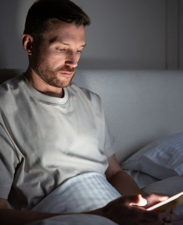 A man using his smartphone in bed at night while his partner sleeps.