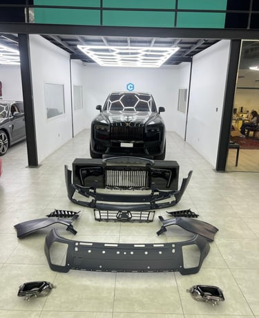 Black Rolls-Royce Cullinan in a luxury auto body shop with disassembled front bumper and grill parts.