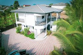 Villa tropicale blanche à douala de deux étages avec balcon, allée pavée et palmiers 