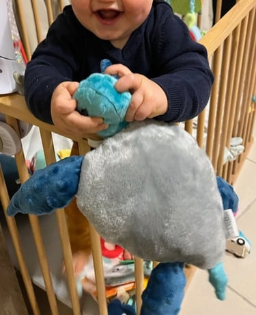 Bébé tenant et manipulant une peluche artisanale dans son lit