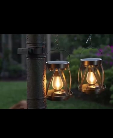 Two decorative bronze solar lanterns with glowing Edison bulbs hanging on a garden post at dusk.