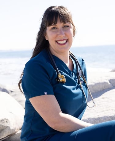 Smiling female healthcare professional wearing blue scrubs and a stethoscope at the beach.