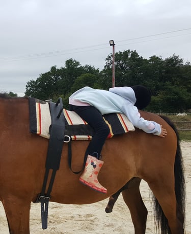 Enfant allongée sur le dos de son cheval lors d'une séance d'équithérapie